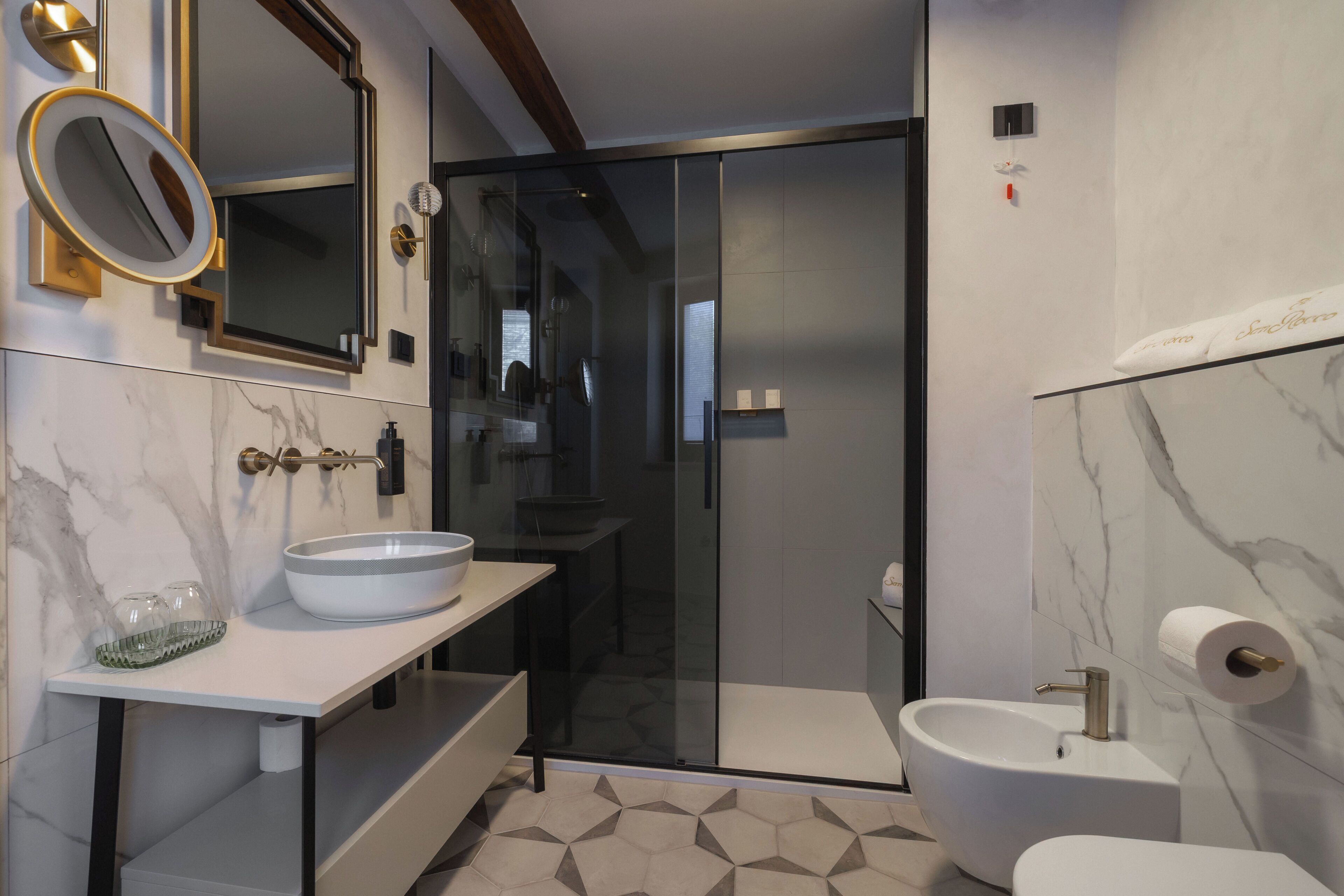 A modern bathroom with a glass-enclosed shower, a white sink, and a marble-tiled floor.