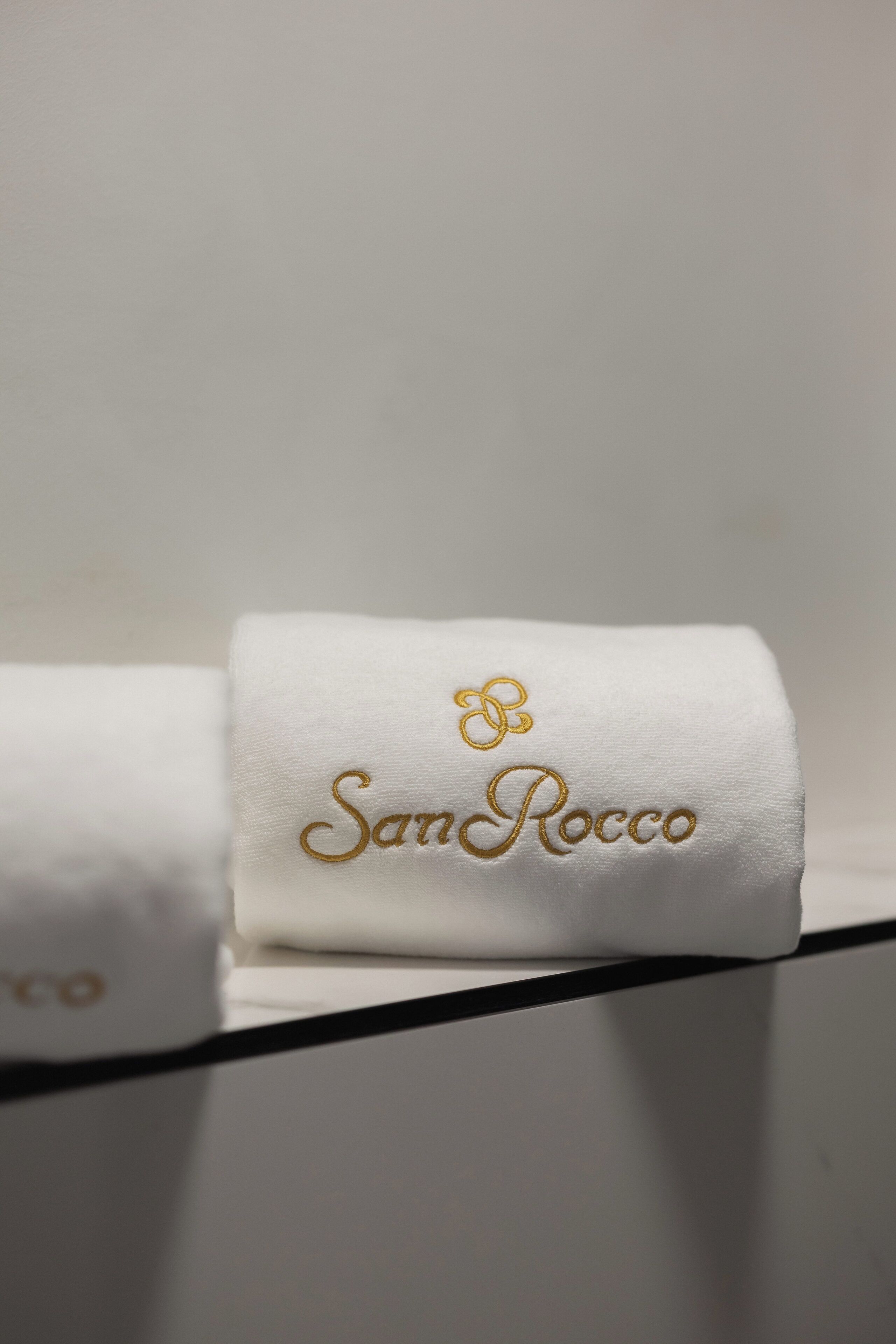 A white towel with 'San Rocco' embroidered in gold.