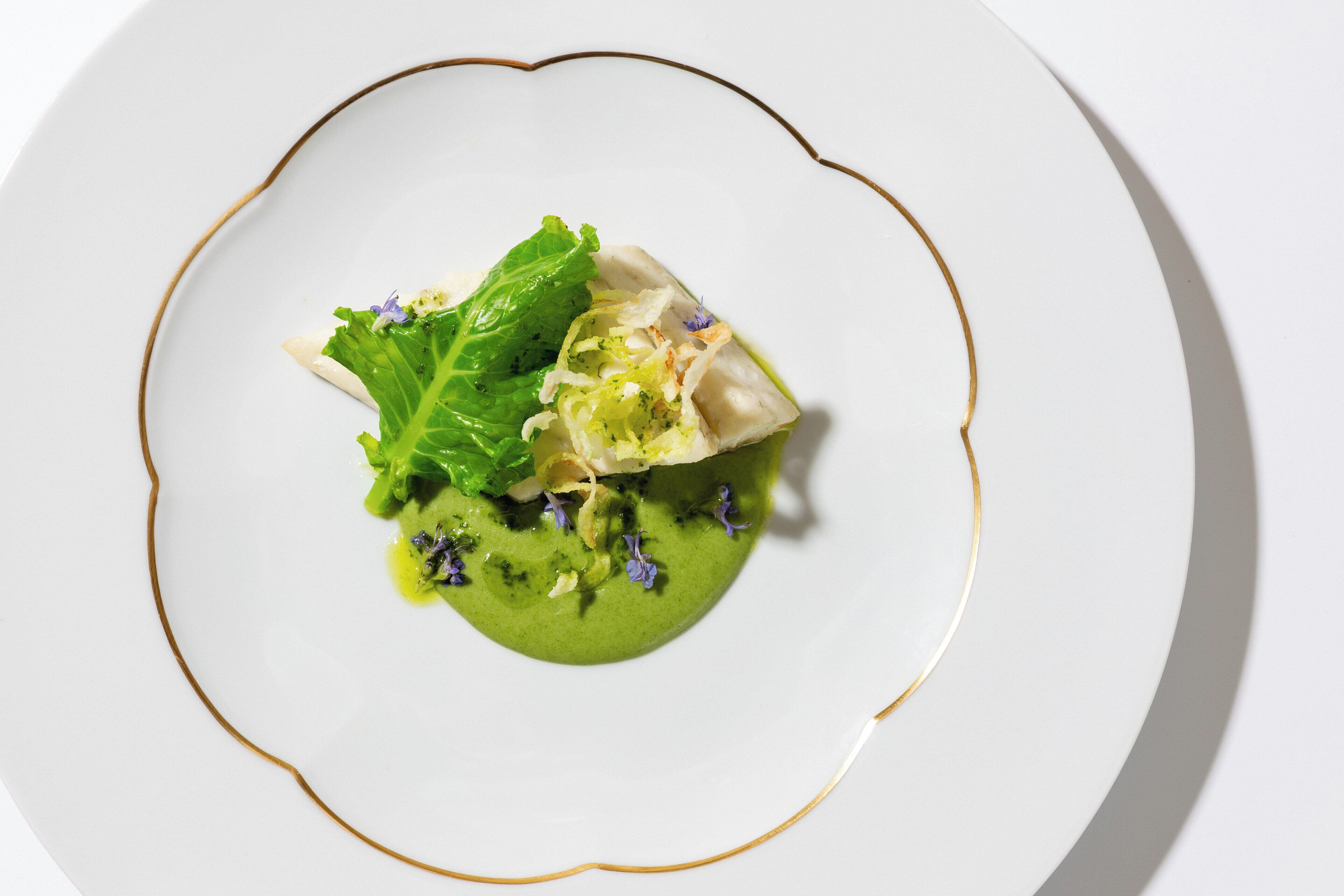 A white plate with a green sauce, a leaf, and a piece of food.