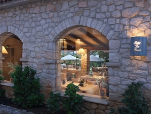 A stone building with arched windows, a sign reading 'Hotel San Rocco,' and outdoor seating with umbrellas.