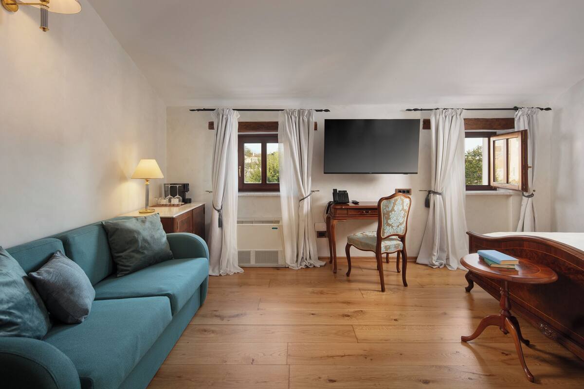 A room with a teal sofa, a wooden desk, a chair, a TV, and a bed.