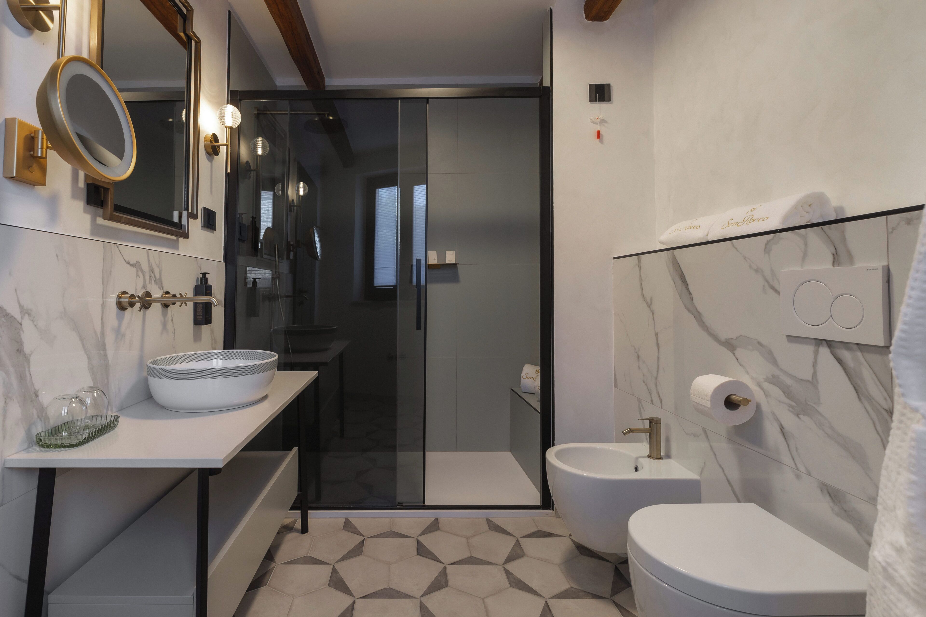 Un baño moderno con cabina de ducha de vidrio, un lavabo blanco con cuenco, un inodoro y paredes con diseño de mármol.