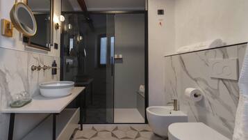Un baño moderno con cabina de ducha de vidrio, un lavabo blanco con cuenco, un inodoro y paredes con diseño de mármol.