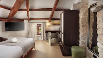 A bedroom with a bed, a desk, a chair, a television, and a stone wall.
