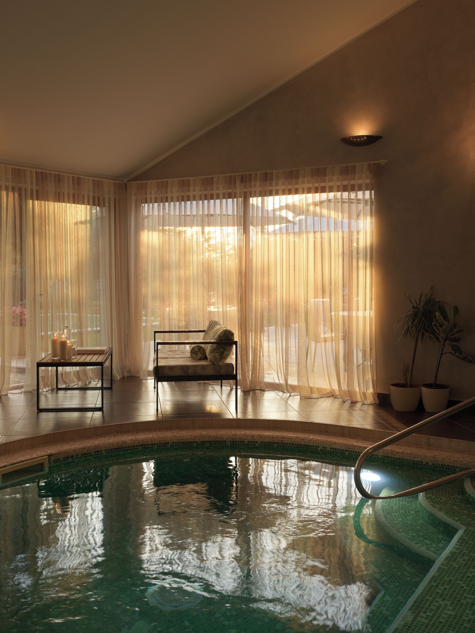 Zona de piscina con una silla, una mesa, una planta en maceta y cortinas translúcidas.