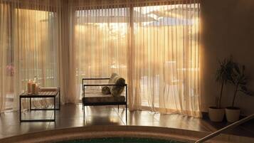 Zona de piscina con una silla, una mesa, una planta en maceta y cortinas translúcidas.