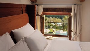 A bedroom with a wooden headboard, white bedding, and a window with a view of an outdoor area. - Heritage Hotel San Rocco (Brtonigla)