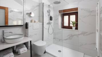 A modern bathroom with a large mirror, a round sink, a toilet, a shower with a glass door, and a small window with a plant.