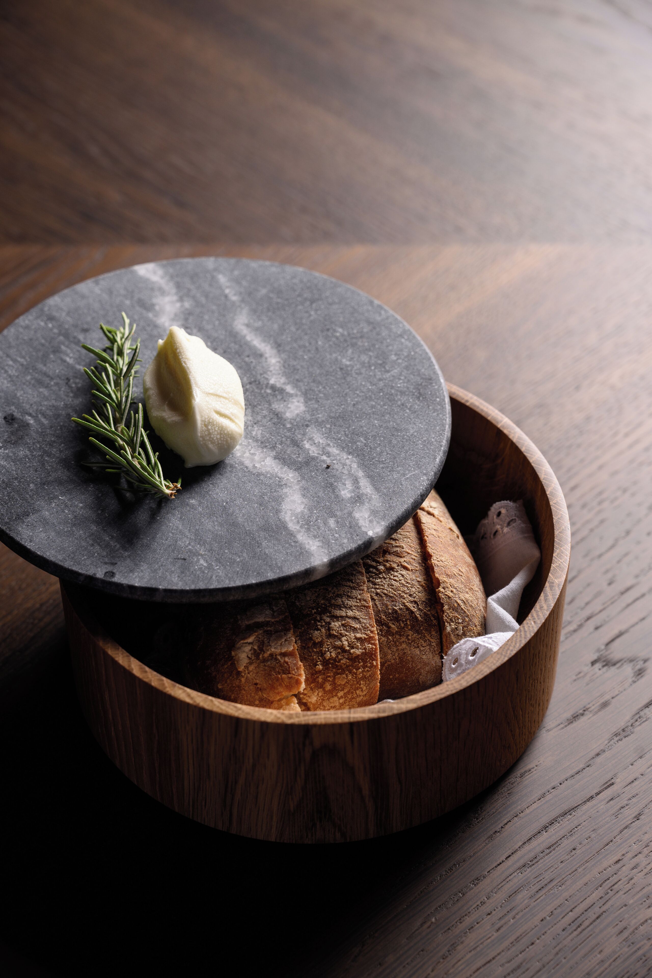 A wooden bowl with bread and a cheese wheel on a slate.