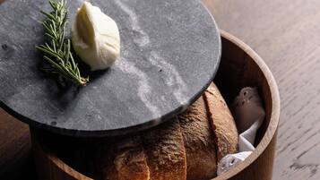 A wooden bowl with bread and a cheese wheel on a slate.