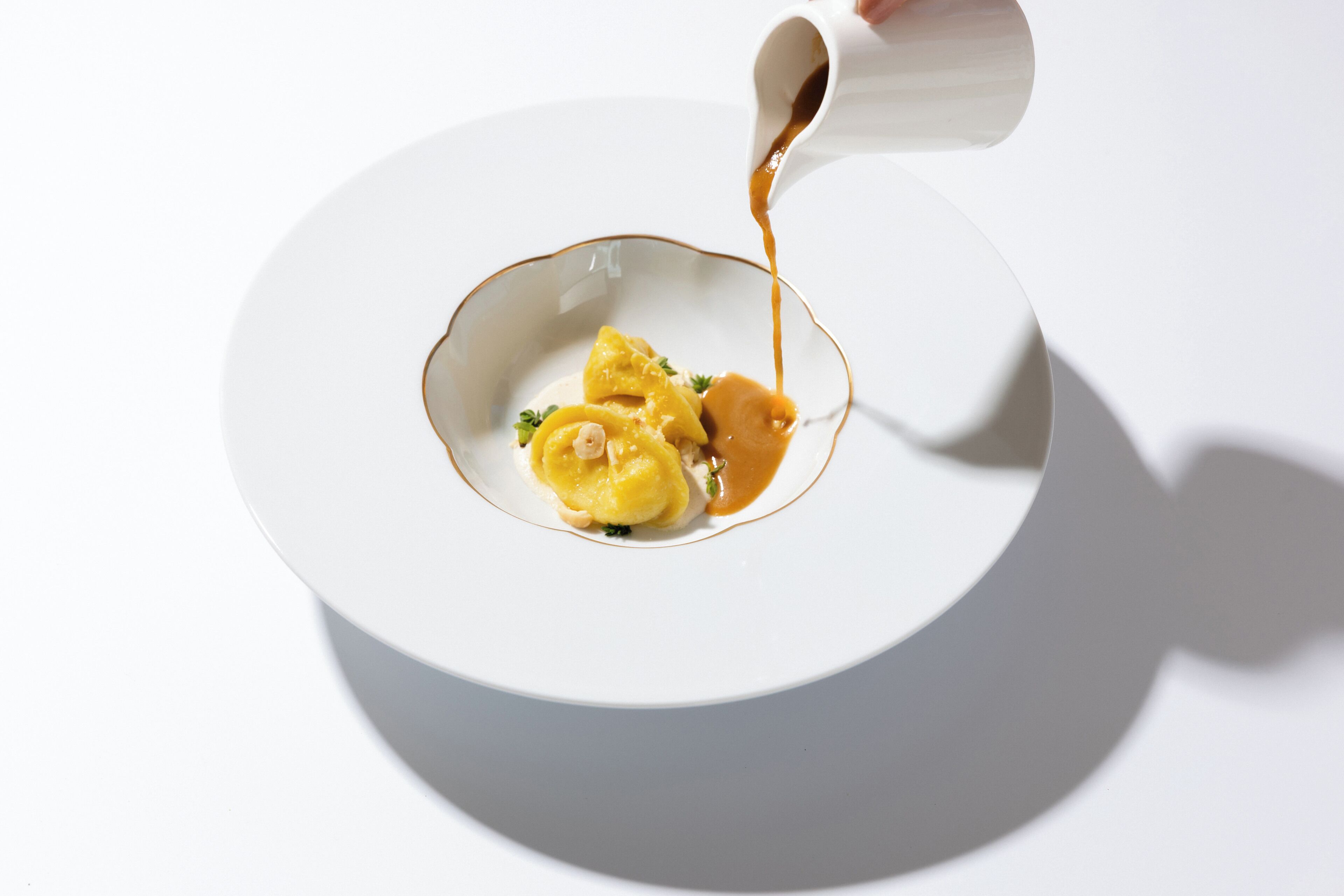 A white plate with a sauce being poured over a food item.