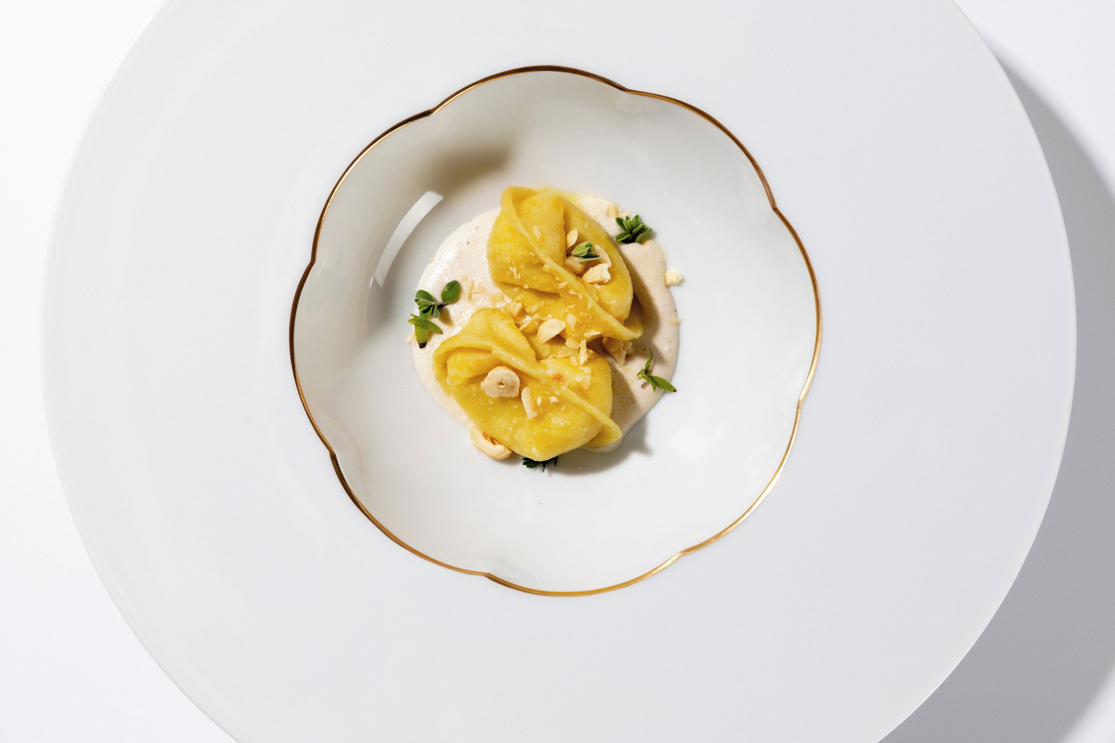 Een wit bord met gouden rand, met een dessert met een romige basis, belegd met geel fruit en versierd met noten en kruiden.