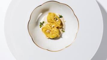 A white plate with a gold rim, containing a dessert with a creamy base, topped with a yellow fruit and garnished with nuts and herbs.