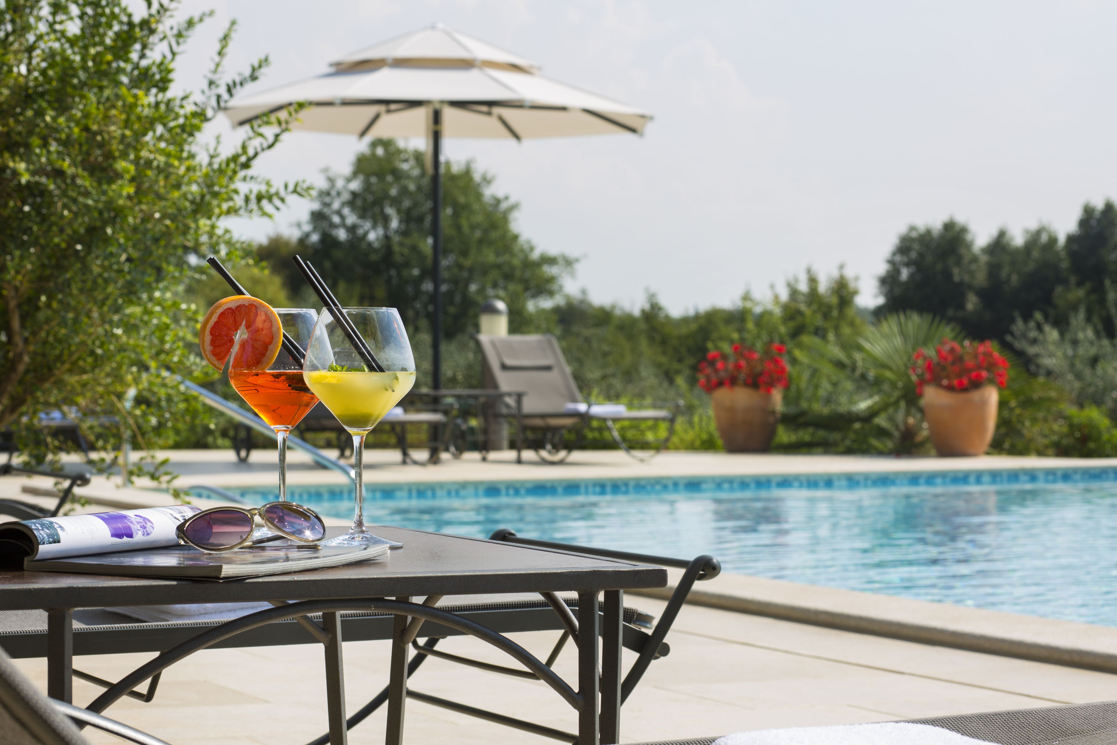 Mesa junto a la piscina con una bebida, gafas de sol y un menú.