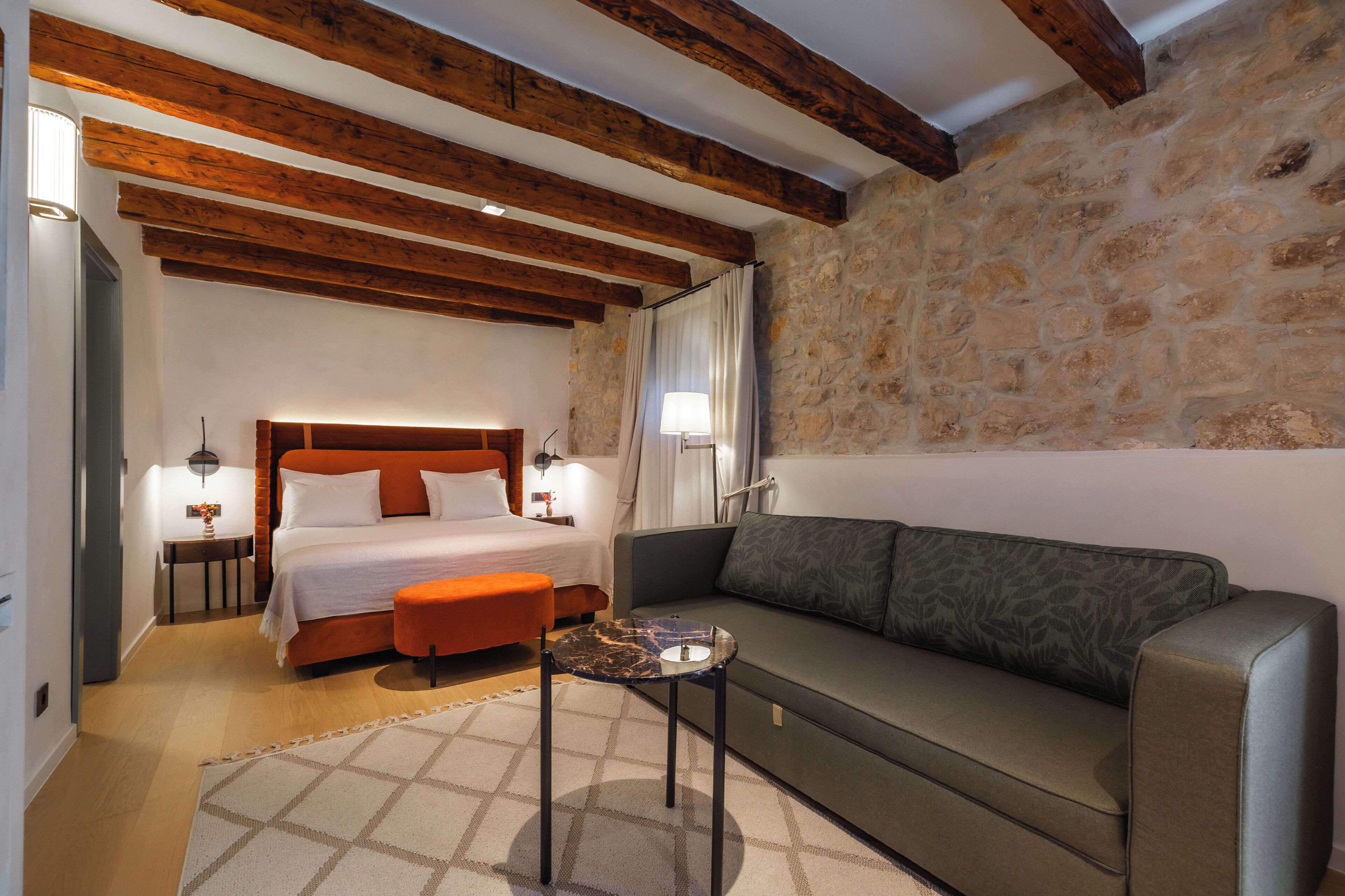 Un dormitorio con cama, sofá, una mesita y pared de piedra.