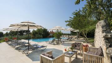 A poolside area with lounge chairs, umbrellas, and a stone wall.