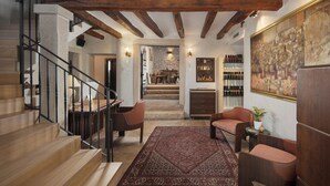 A wooden staircase leading to a dining area with a red patterned rug, a seating area with chairs, and a wall-mounted wine rack. - Heritage Hotel San Rocco (Brtonigla)