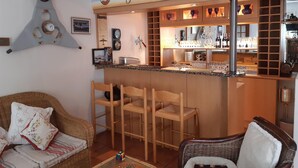 Un rincón de bar acogedor con un mostrador de madera, taburetes y una gran variedad de copas y botellas.