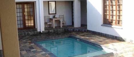 Piscina com ladrilhos de pedra, um alpendre coberto com mesa e cadeiras, e uma janela tradicional japonesa.