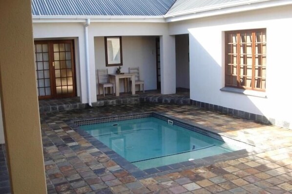 Una piscina con baldosas de piedra, un porche cubierto con mesa y sillas, y una ventana de estilo japonés tradicional.