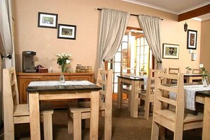 A dining area with wooden tables and chairs, a coffee machine, and framed pictures on the walls. - Baleia Guest Lodge Bed & Breakfast (Hermanus)