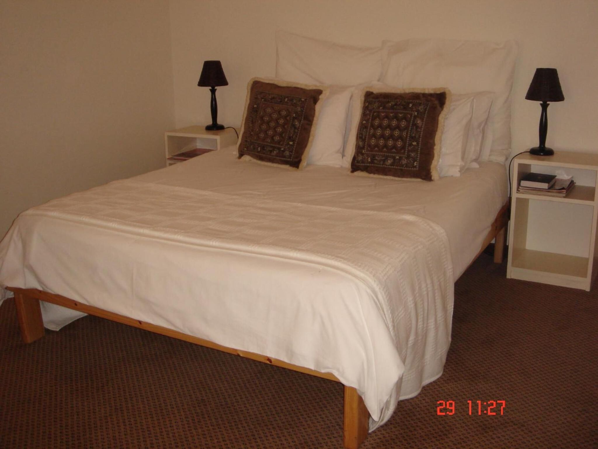 Una cama individual con ropa de cama blanca, dos mesitas de noche con lámparas y almohadones estampados.