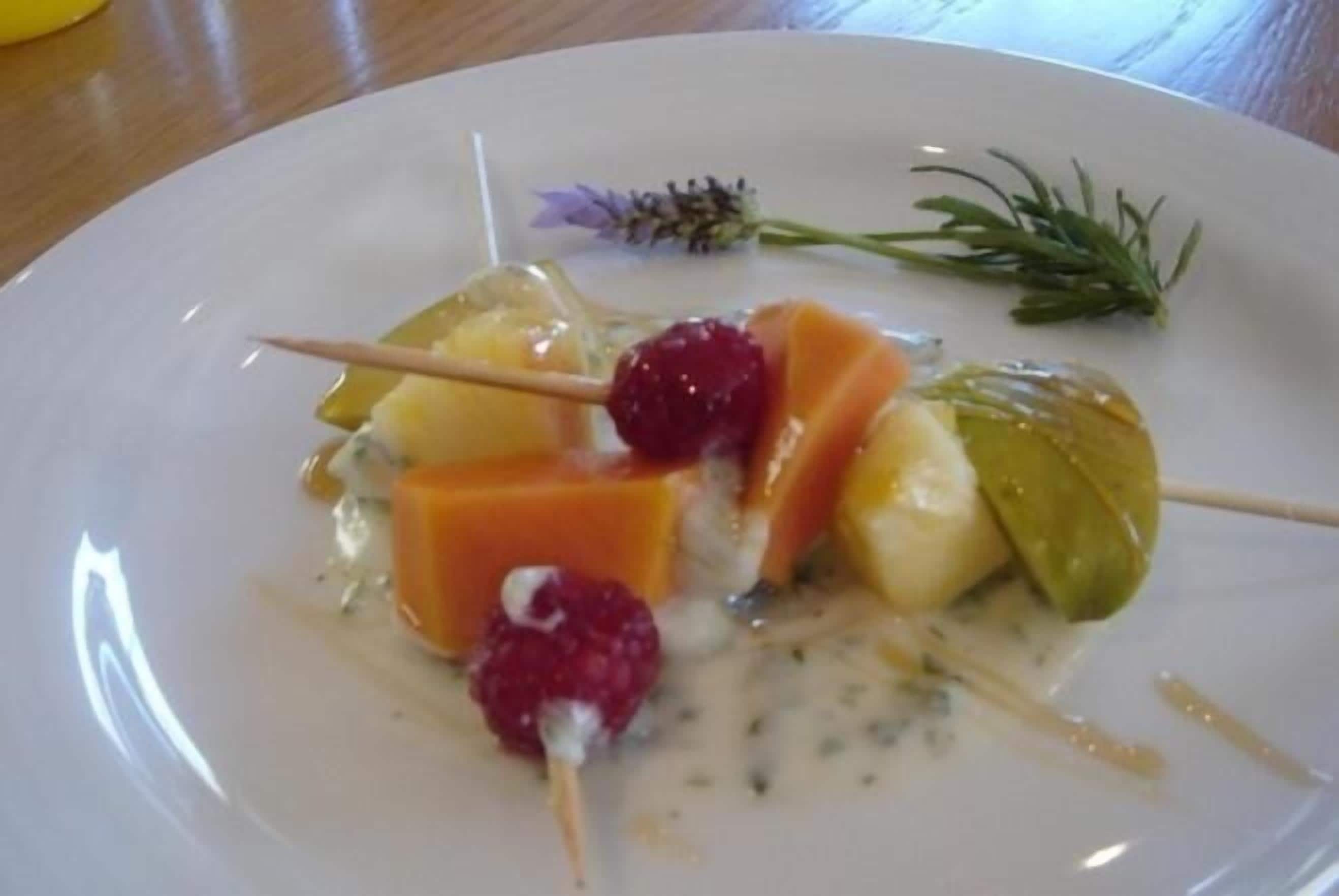A plate with a dessert consisting of fruit and a creamy sauce, garnished with a sprig of rosemary.