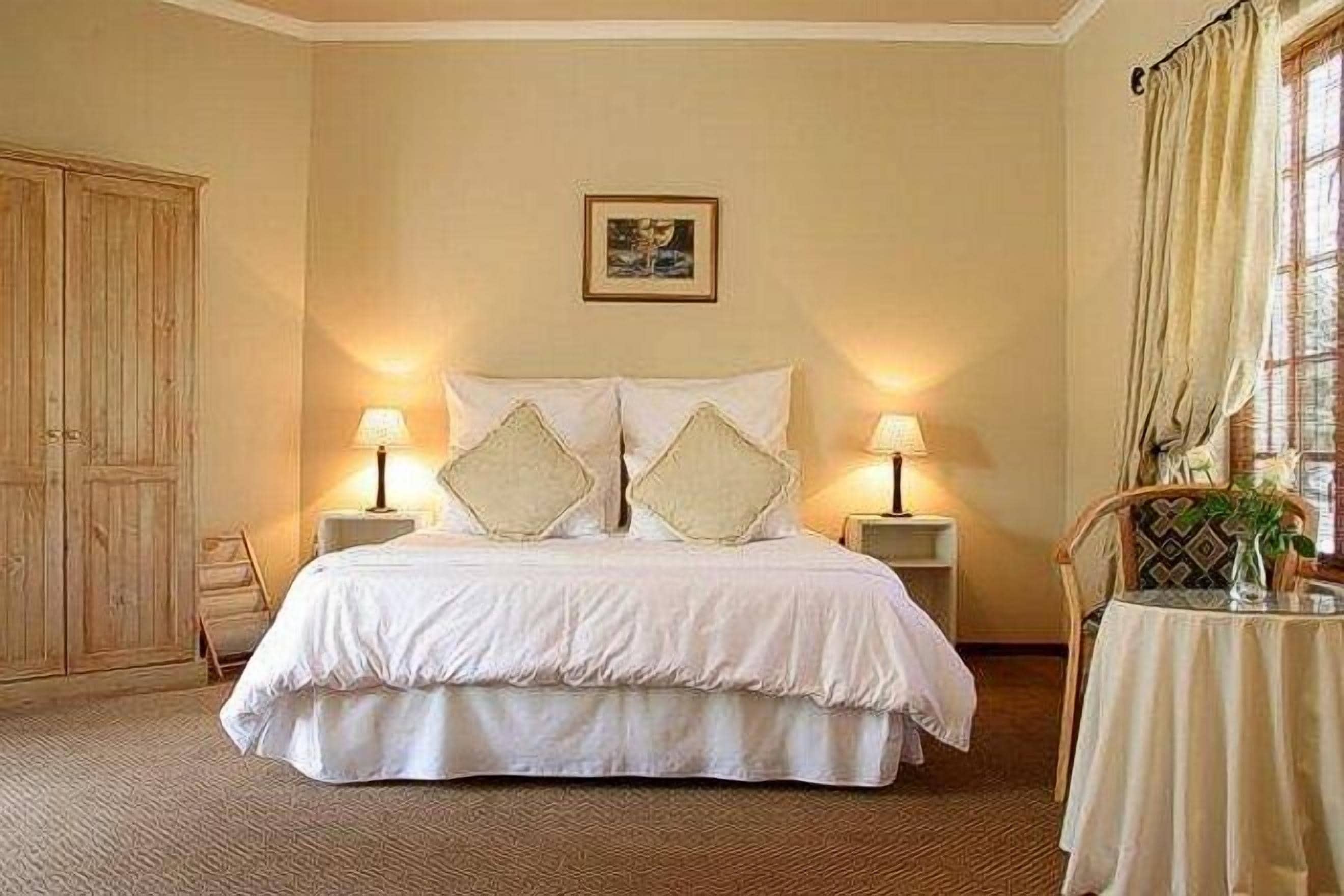 A hotel room with a large bed, two bedside lamps, a framed picture on the wall, and a window with curtains.