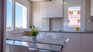 Une cuisine moderne avec des meubles blancs, une table à manger avec des chaises, une plante en pot et une vue par la fenêtre.