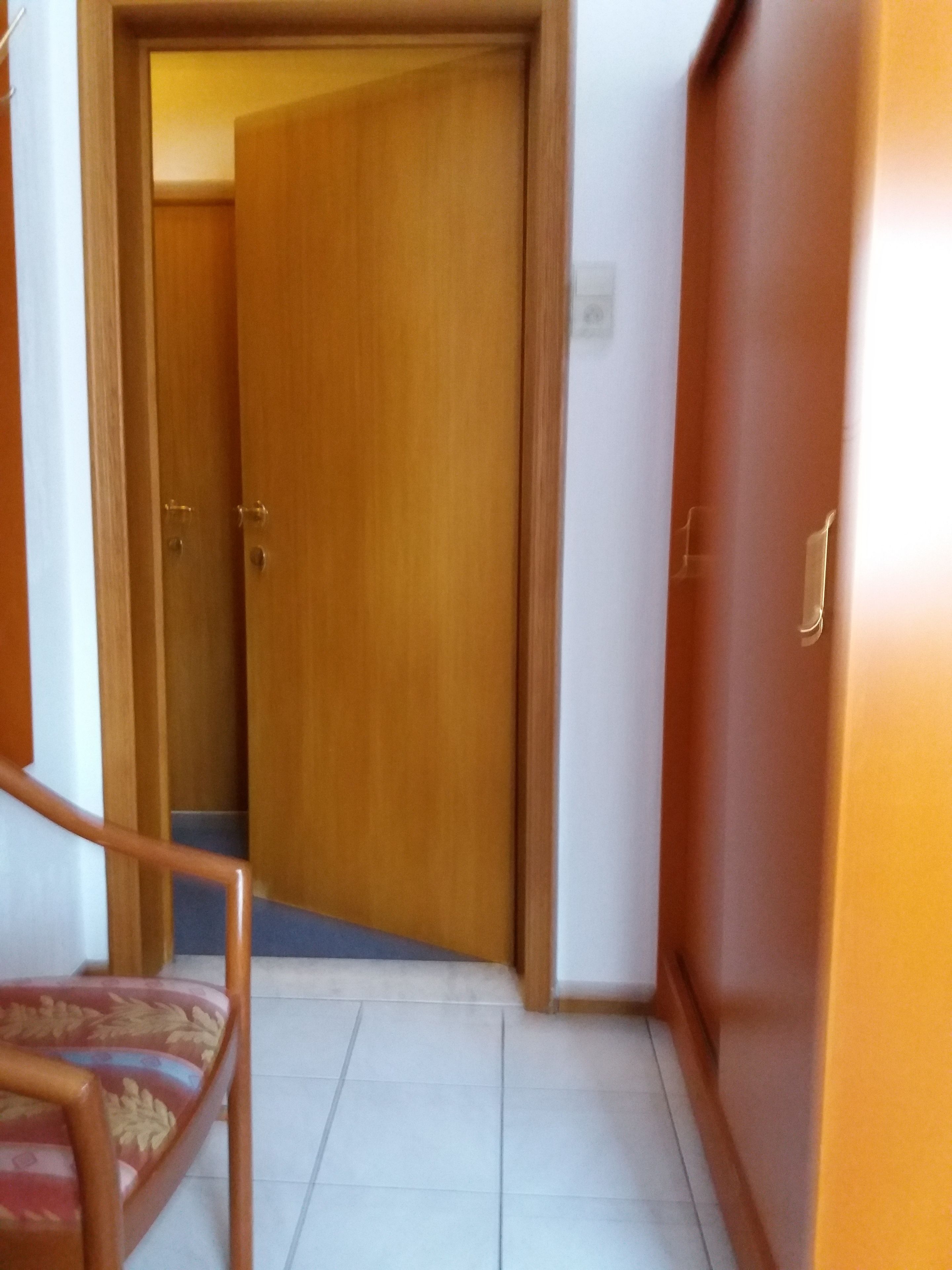 Un pasillo con una puerta de madera, piso de baldosas y un armario de madera.