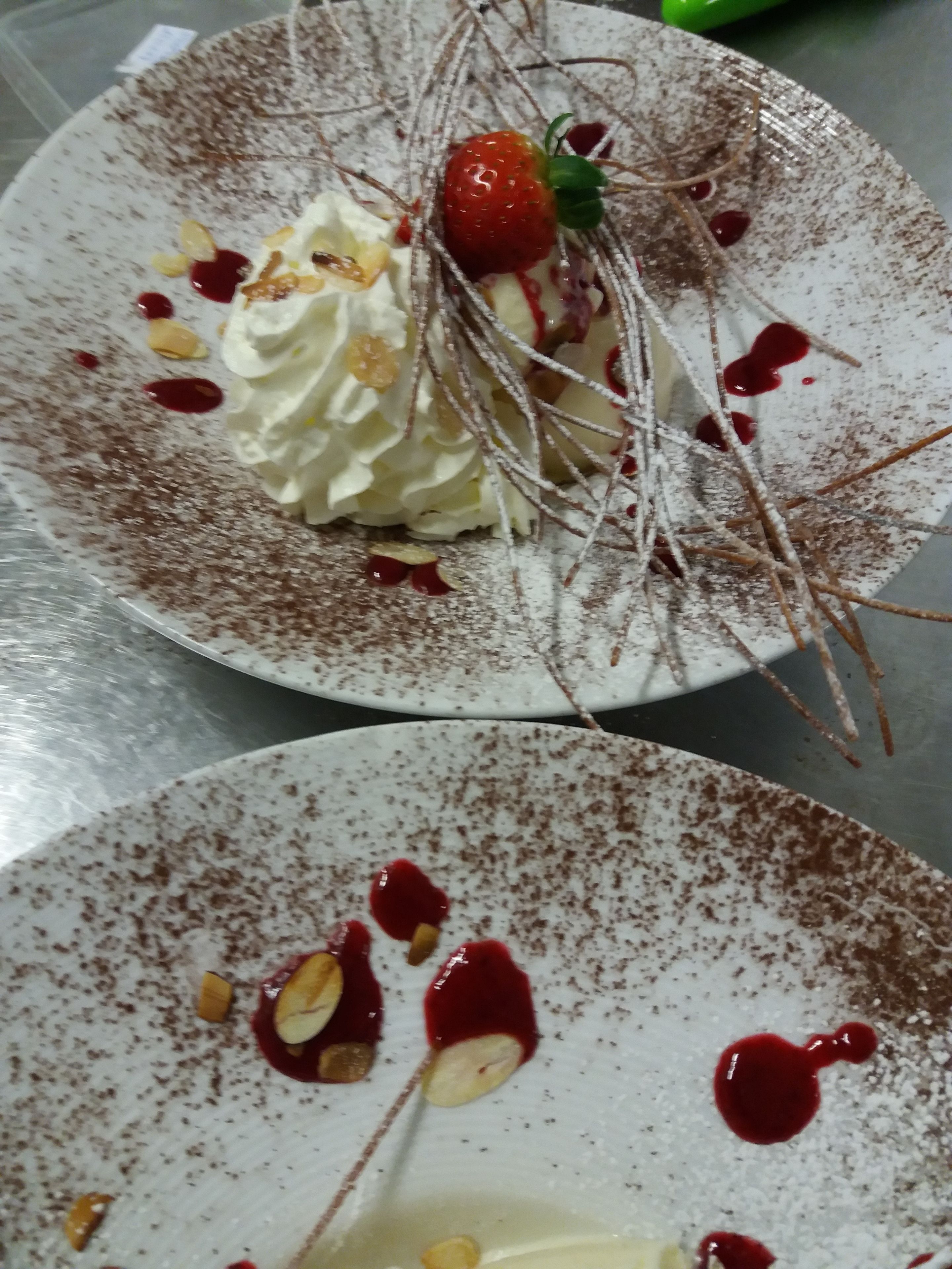 A dessert with whipped cream, strawberries, and chocolate shavings on a plate.