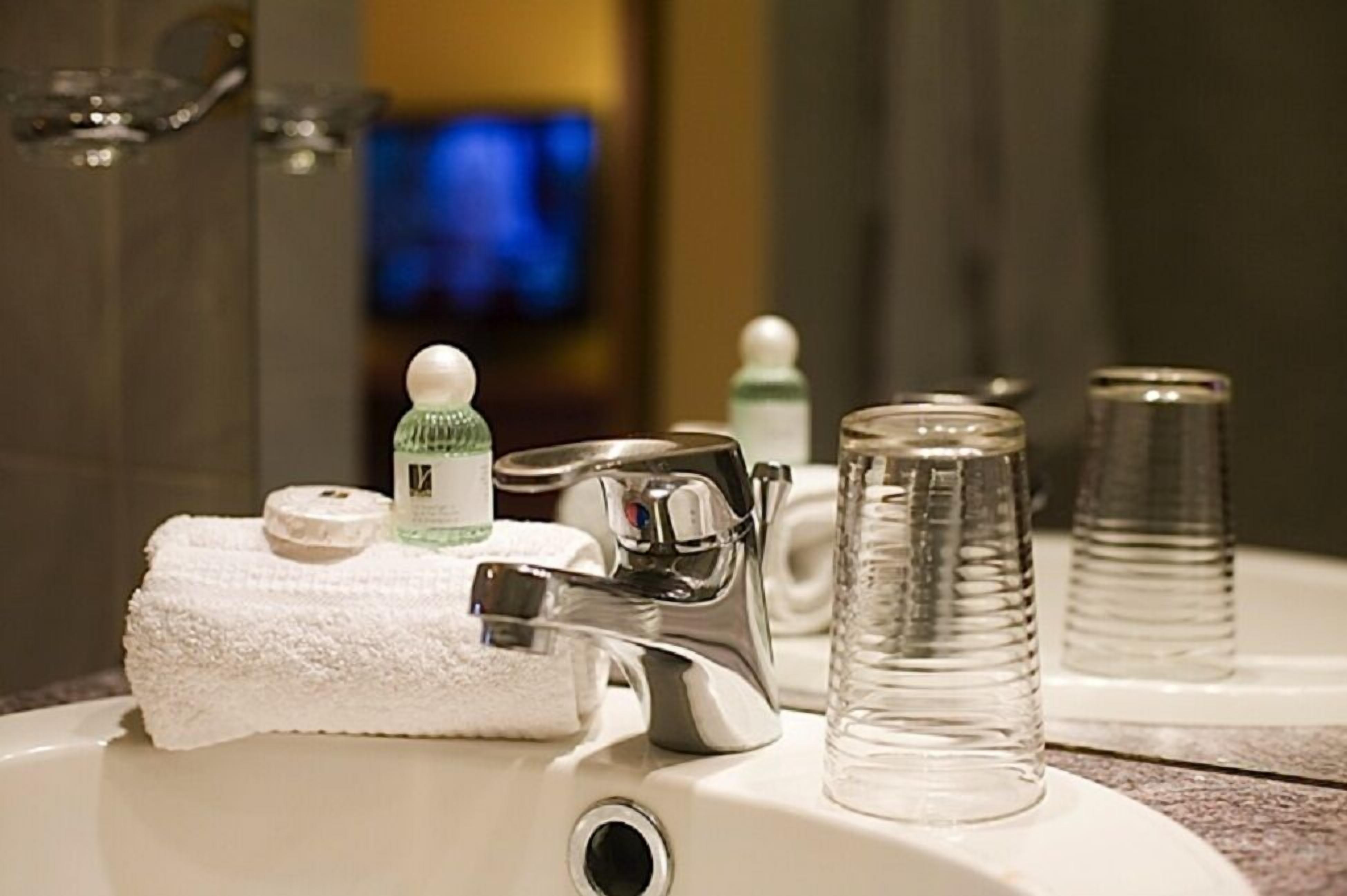 A bathroom sink with a white towel, a soap dispenser, a glass, and a faucet.