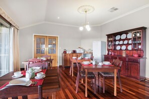 Ein Essbereich mit Holztischen und -stühlen, eine Küche mit Schränken und Geräten sowie ein dekorativer Schrank mit Geschirr.