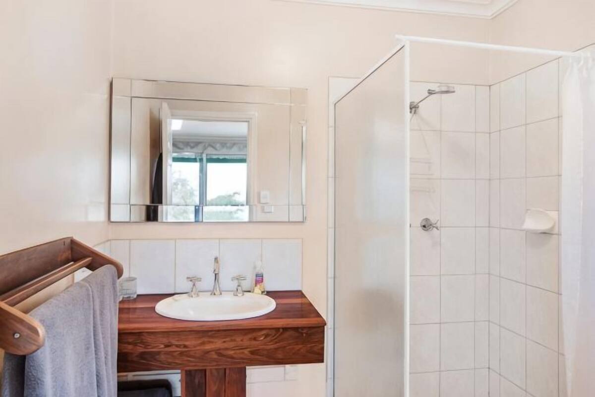 Ein Badezimmer mit einem Holzkosmetikschrank, einem weißen Waschbecken, einem Spiegel und einer Duschkabine.