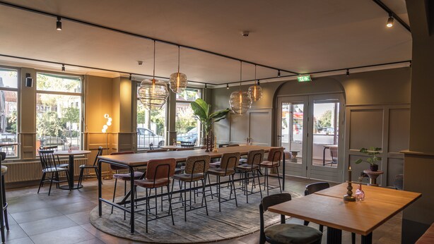 A restaurant with a central bar, multiple seating areas, and large windows offering views of the street. - Het Hart van Weesp (Weesp)