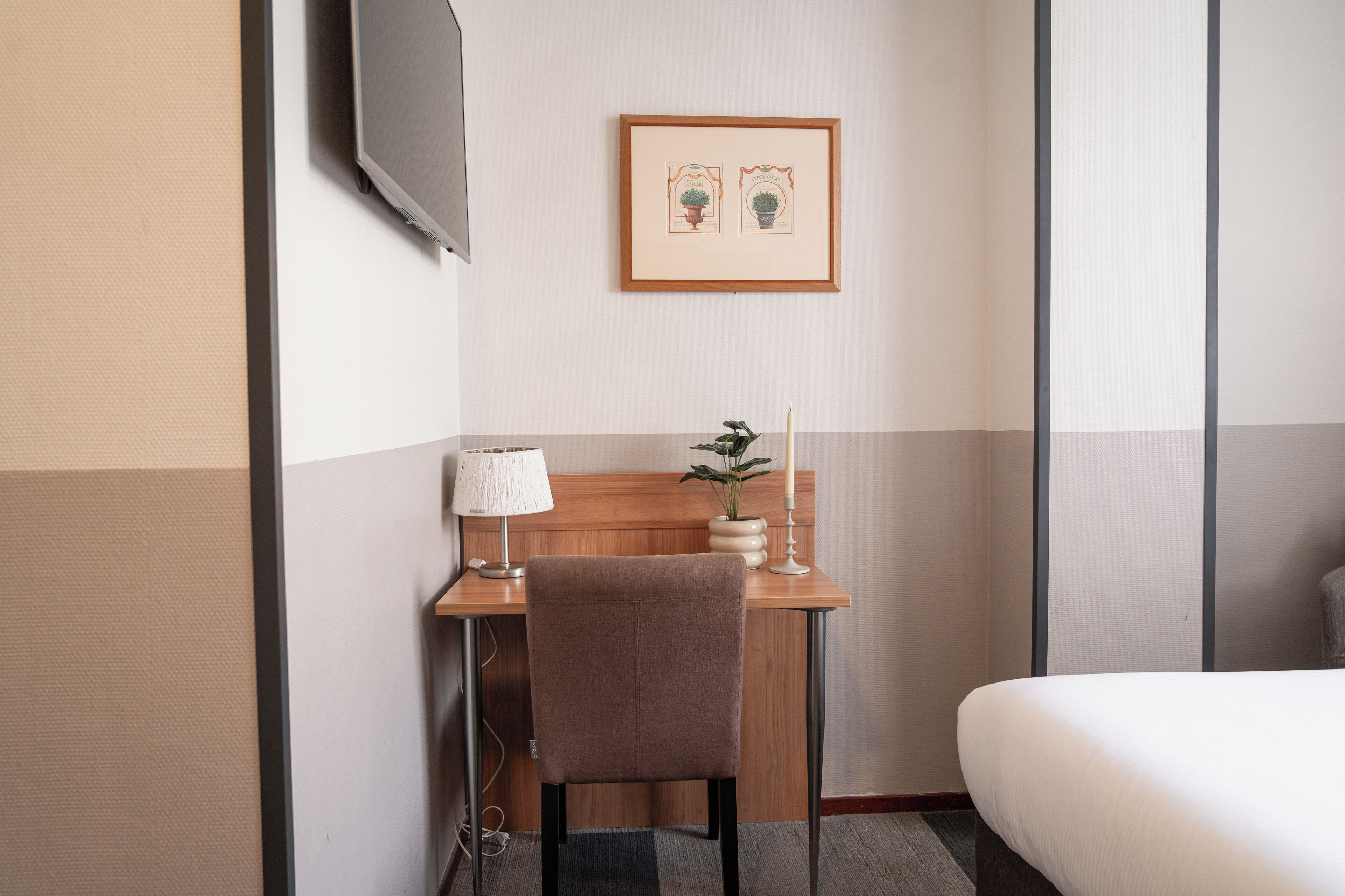 Een hotelkamer met een bed, een bureau met stoel, een aan de muur bevestigde televisie en een lijst boven het bureau.