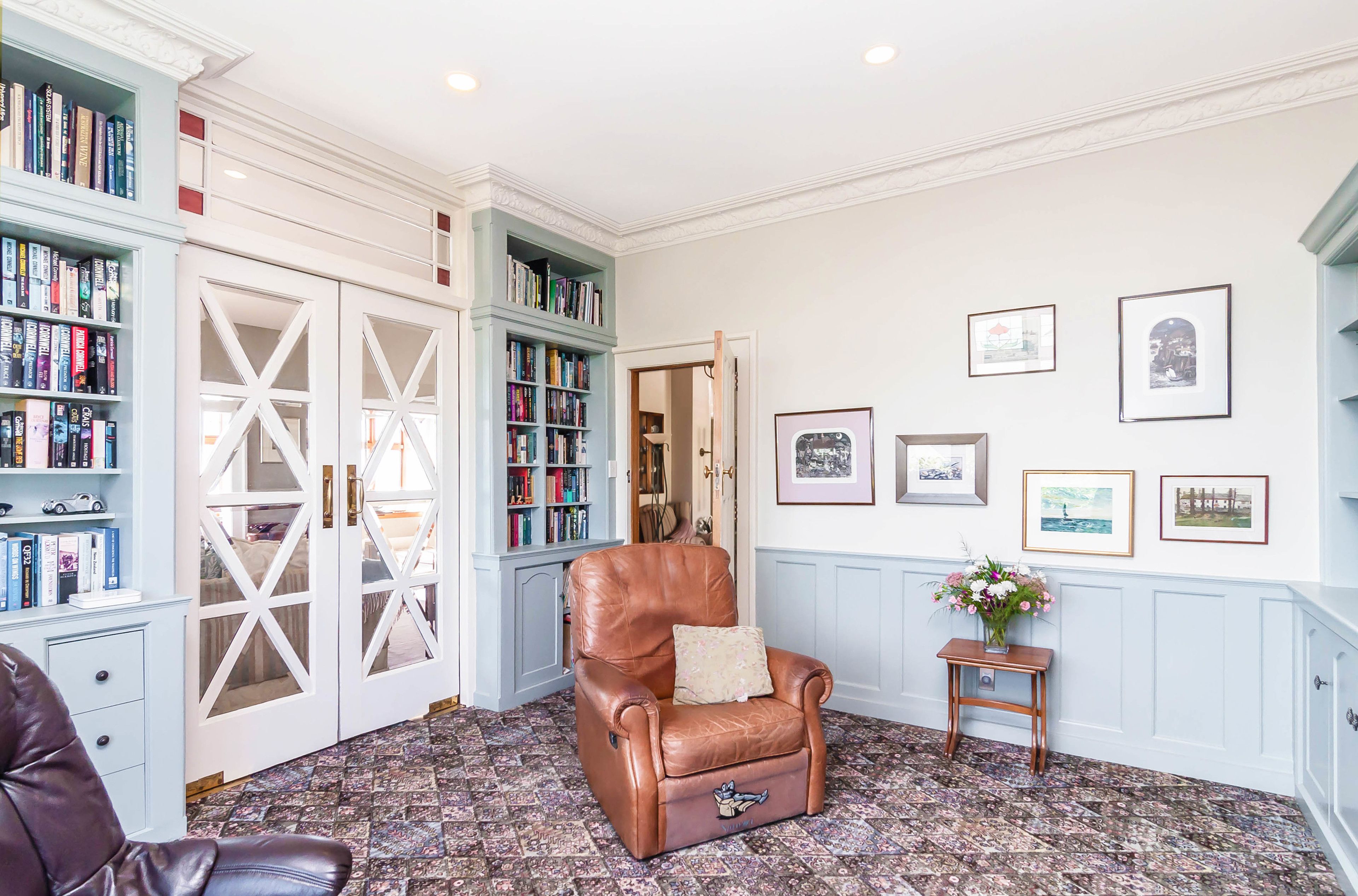 Una habitación con un sillón de cuero marrón, una estantería y cuadros enmarcados en la pared.