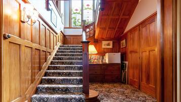 A wooden staircase with patterned carpet, a wooden handrail, and a view of a room with a refrigerator and a window with stained glass.