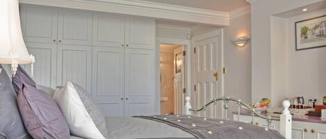 Un dormitorio con cama, mesita de noche, lámpara y cómoda. Se ve una puerta que da a otra habitación.