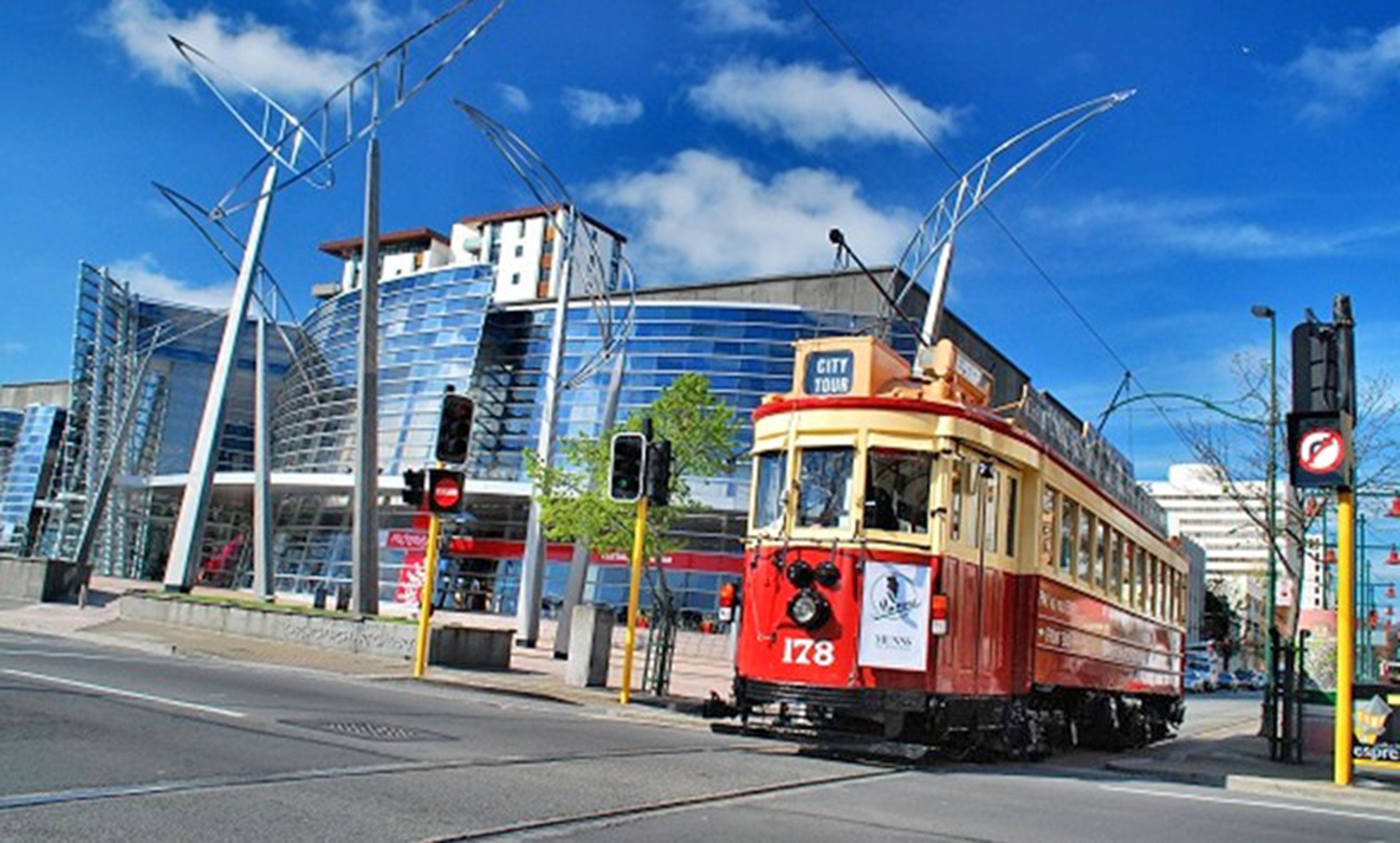 Un tranvía rojo y amarillo en una intersección urbana, con edificios modernos al fondo.