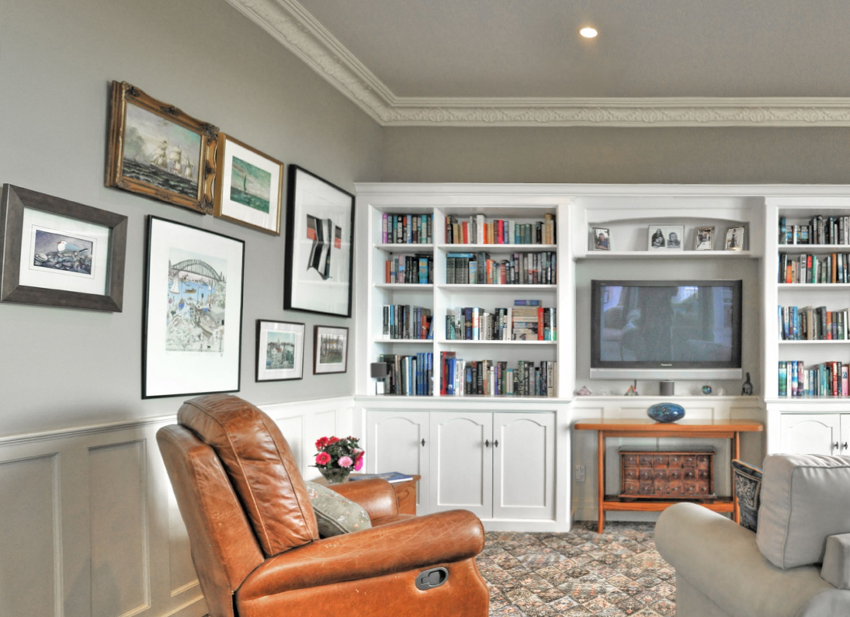 A living room with a leather armchair, a sofa, a fireplace, a television, and a bookshelf filled with books.