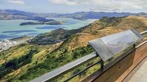 A panoramic view of a coastal landscape with a clear sky, featuring a prominent mountain range, a body of water, and a distant town.