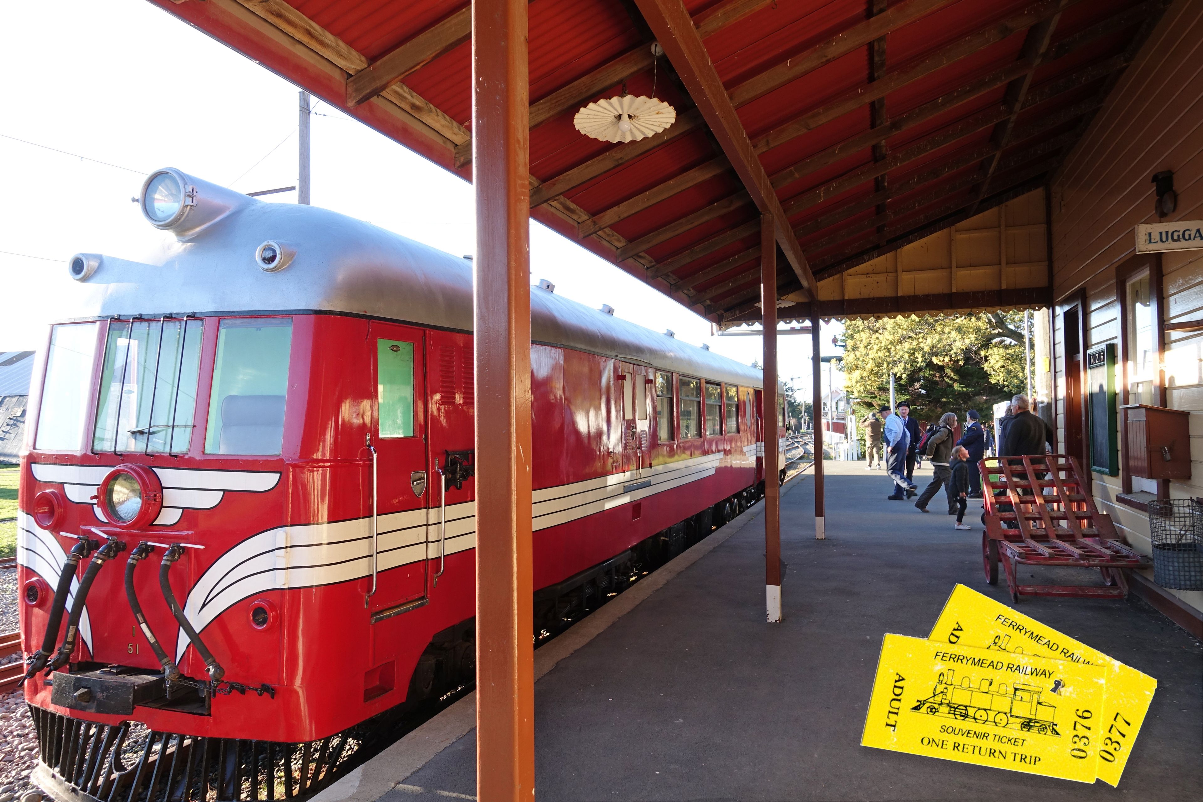 A red and white vintage train at a station platform with a covered waiting area and a signboard.