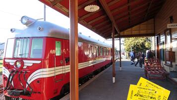 A red and white vintage train at a station platform with a covered waiting area and a signboard.