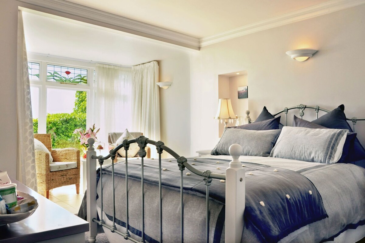A bedroom with a bed, a chair, a table, a lamp, and a window with curtains.