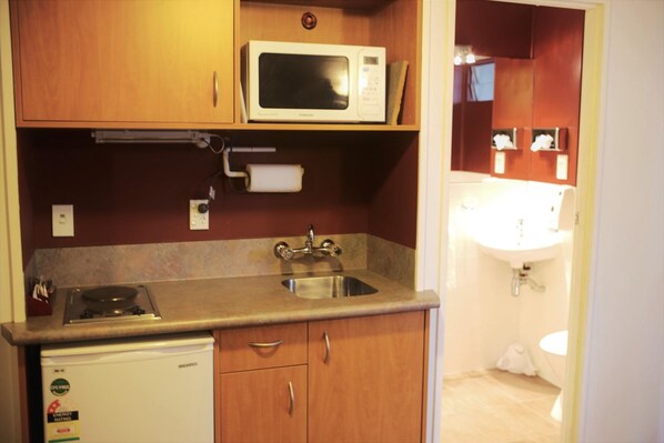 Una cocina compacta con microondas, fregadero y un refrigerador pequeño.