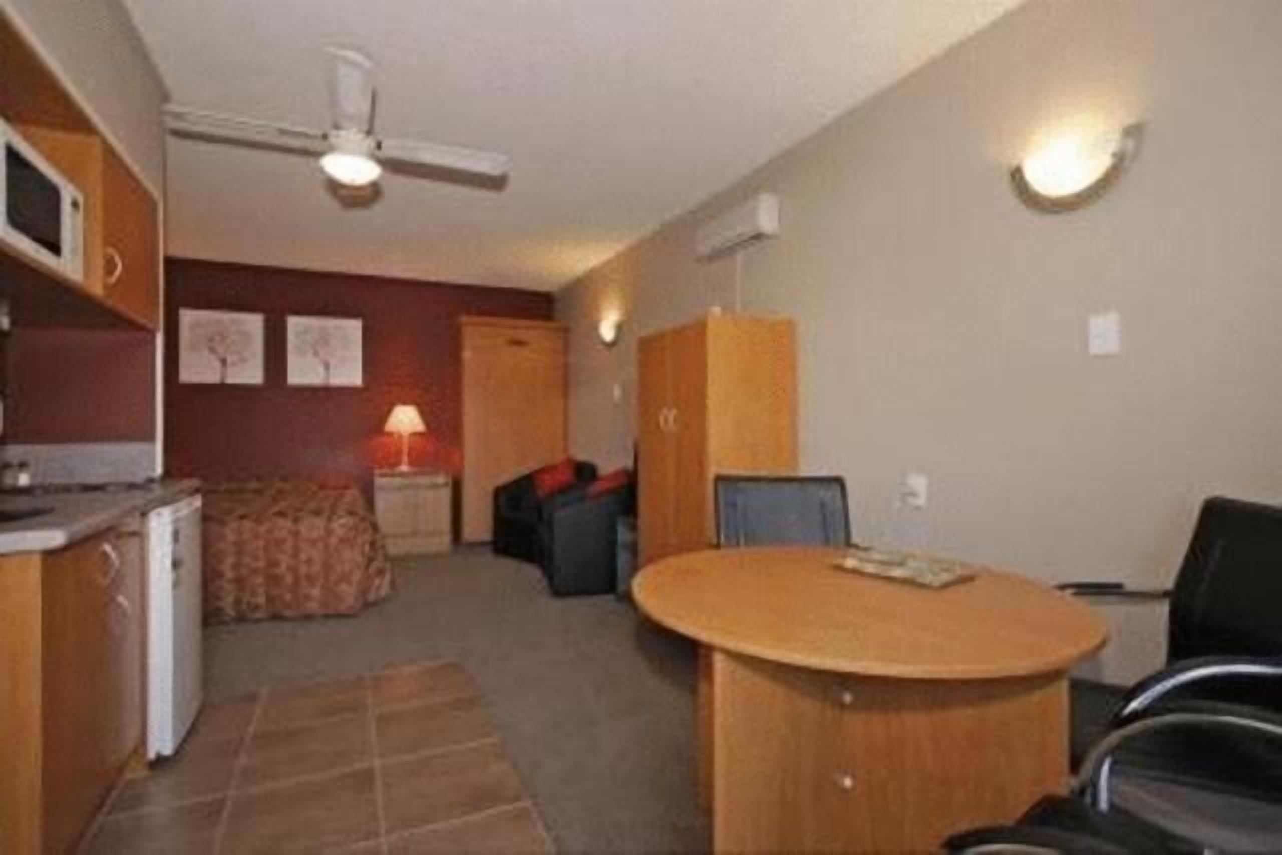 Een kleine kamer met een kitchenette, een ronde eettafel, een plafondventilator en een wandlamp.