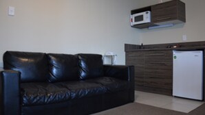 A black leather sofa, a microwave, and a refrigerator in a modern kitchen area. - Kiwi Studios Motel (Palmerston North)