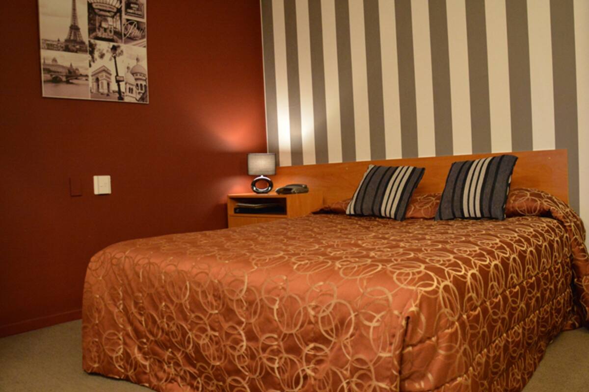 A bedroom with a large bed, striped wallpaper, and a nightstand with a lamp.