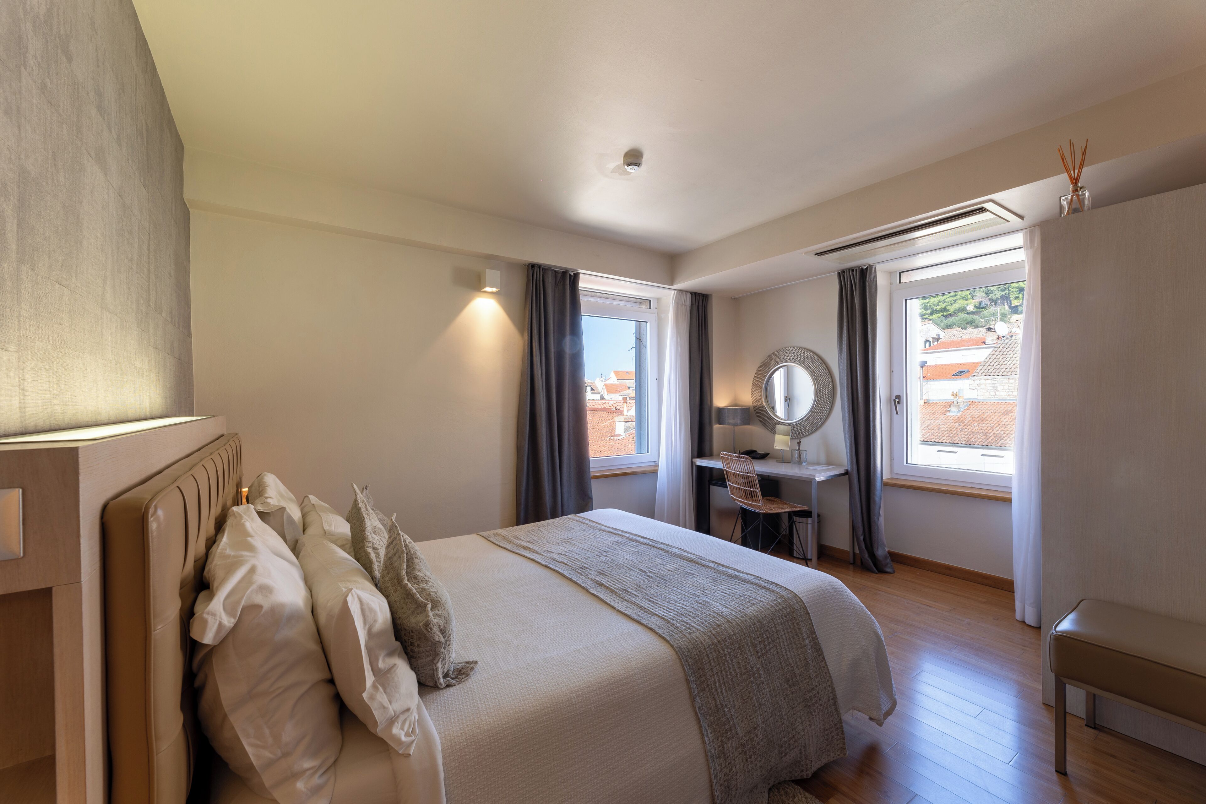 Une chambre à coucher avec un lit, un bureau, une chaise, un miroir et une fenêtre avec des rideaux.